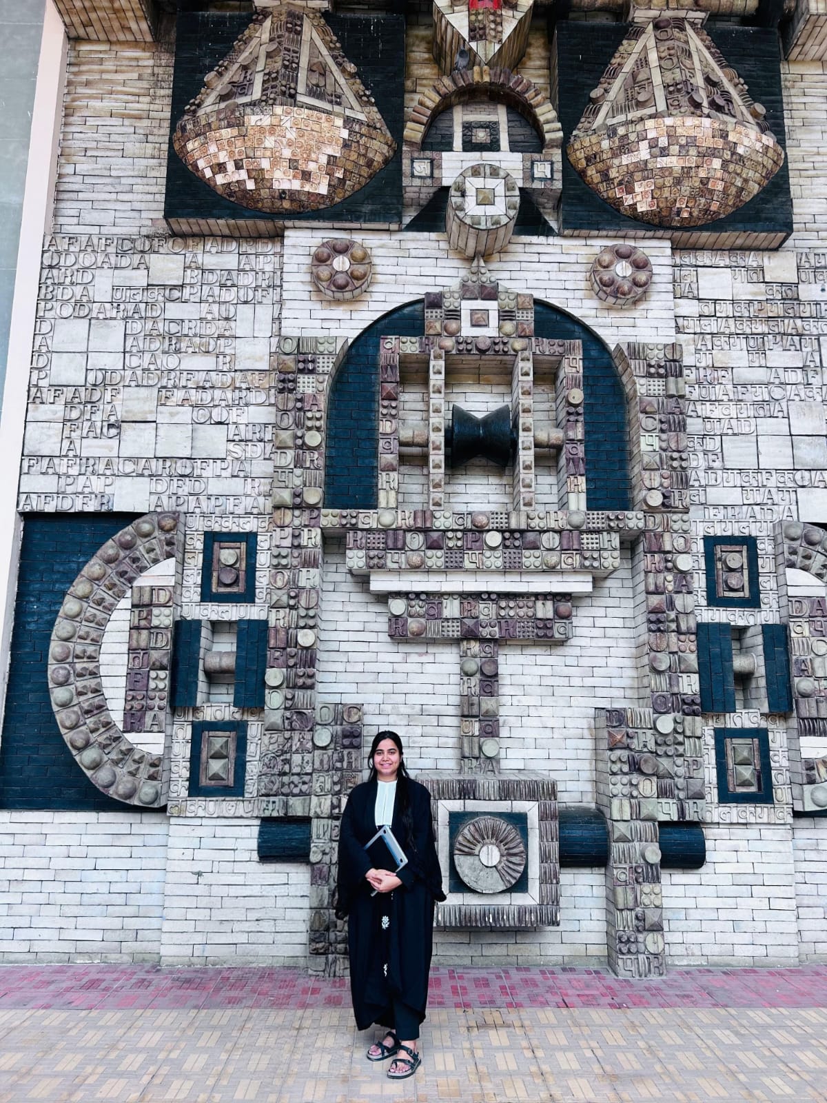 Himani Kalra standing in front of a patterned stone wall